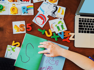 Tools for learning the alphabet on a table and a child writing in a notebook.
