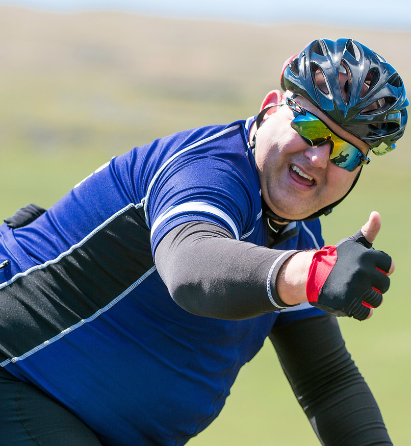 Persona en bicicleta vestida de azul con negro y casco que hace una seña de "OK"