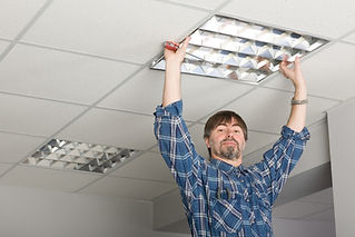 Electrician installs lighting to the ceiling in the office