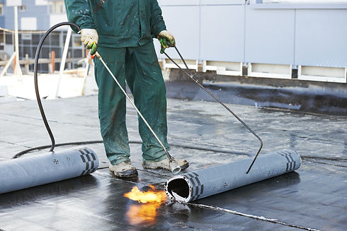 Roofer installing the roofing felt with heating and melting of bitumen roll