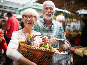 A retired couple show off their baskets of fresh fruits and vegetables from a local farmer's market.