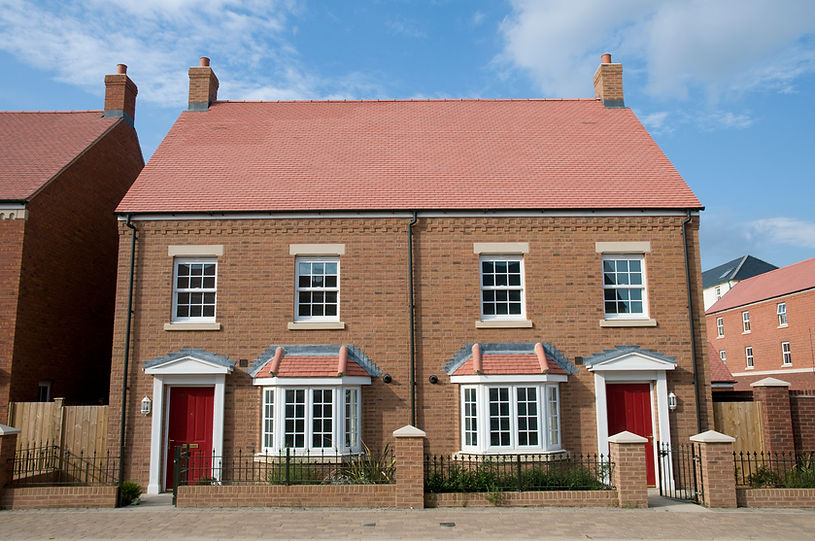 Two identical brick houses with red roofs and red doors, each with a white-framed window