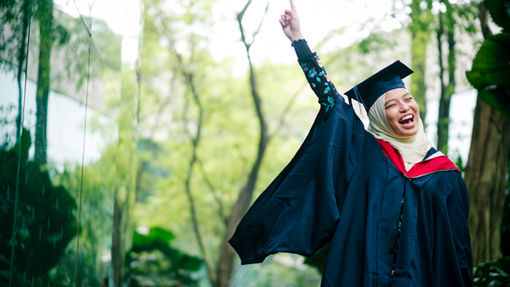 Young woman wearing a graduation gown and cap, smiling proudly outdoors, symbolizing educational achievement and the successful use of a 529 plan.