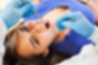 A woman in a blue shirt lies on a dental chair with her mouth open