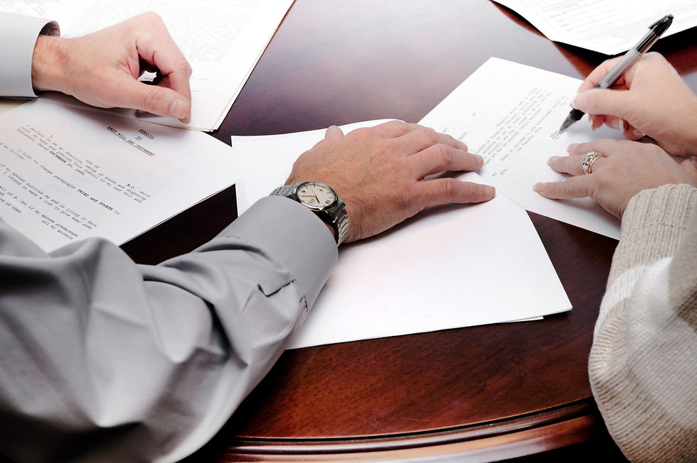 A woman signing a legal document alongside a professional at a wooden table.