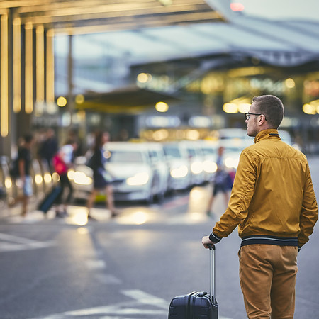 Rear view of a man with luggage standing on the street at the airport