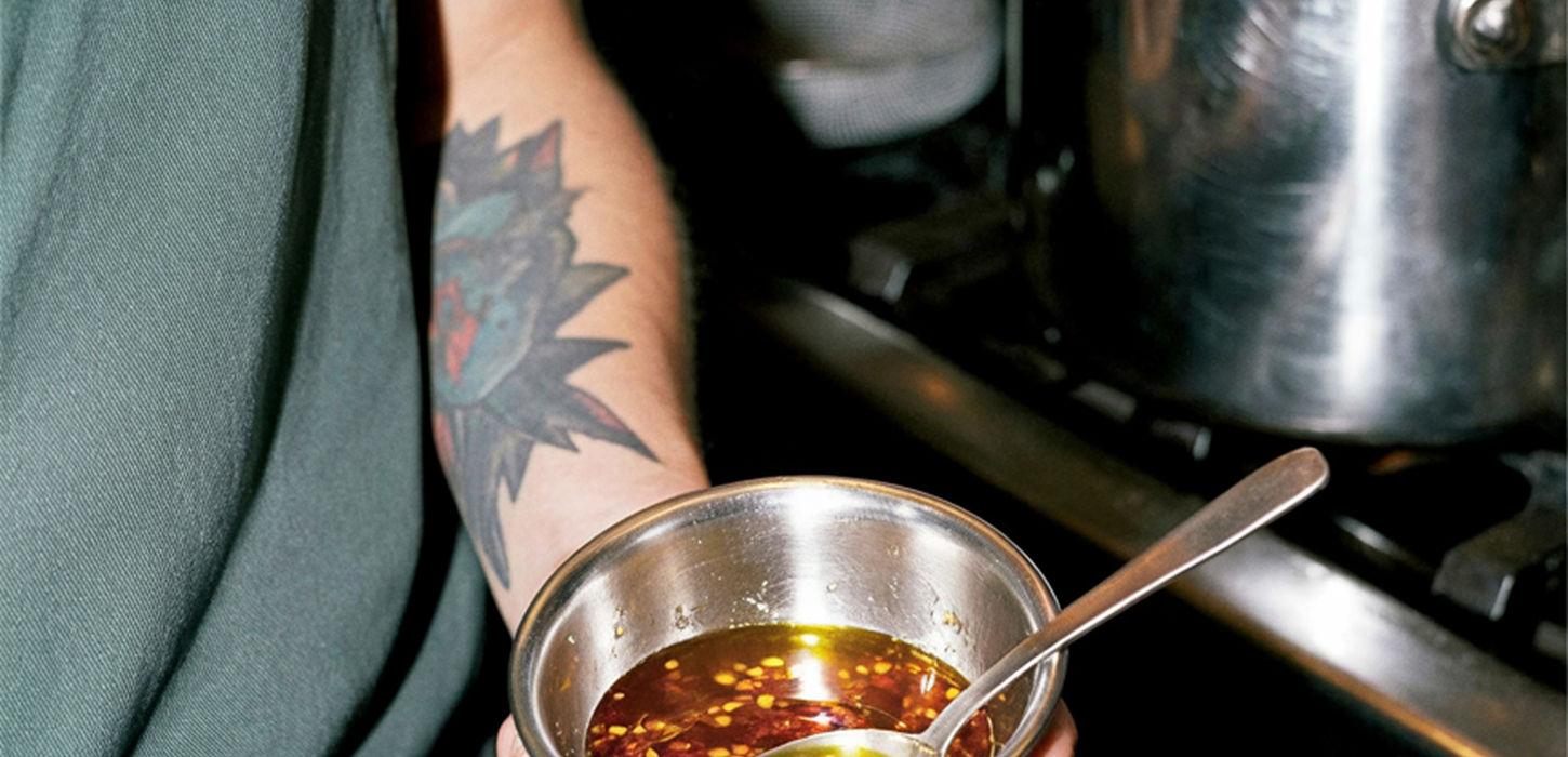 Chef holding a bowl of chili oil near a stove