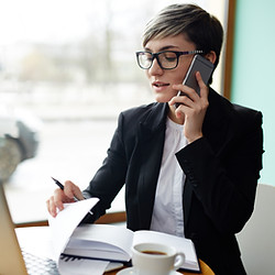 Frau von vorne sichtbar, schaut telefonierend Dokumente an einem Tisch durch