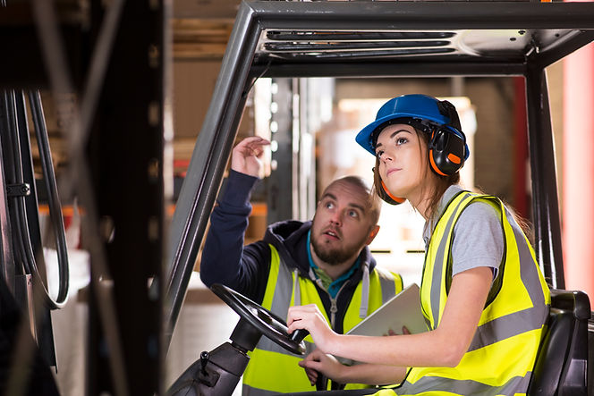 Close-up of two workers in high-visibility vests sitting in a forklift cab, one holding a tablet and the other's hand on the steering wheel