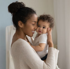 a mother smiling while holding her 6 month old baby in her arms. Baby's face is touching moms.
