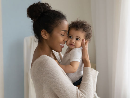 a woman holding her baby near in front of a window with white shades