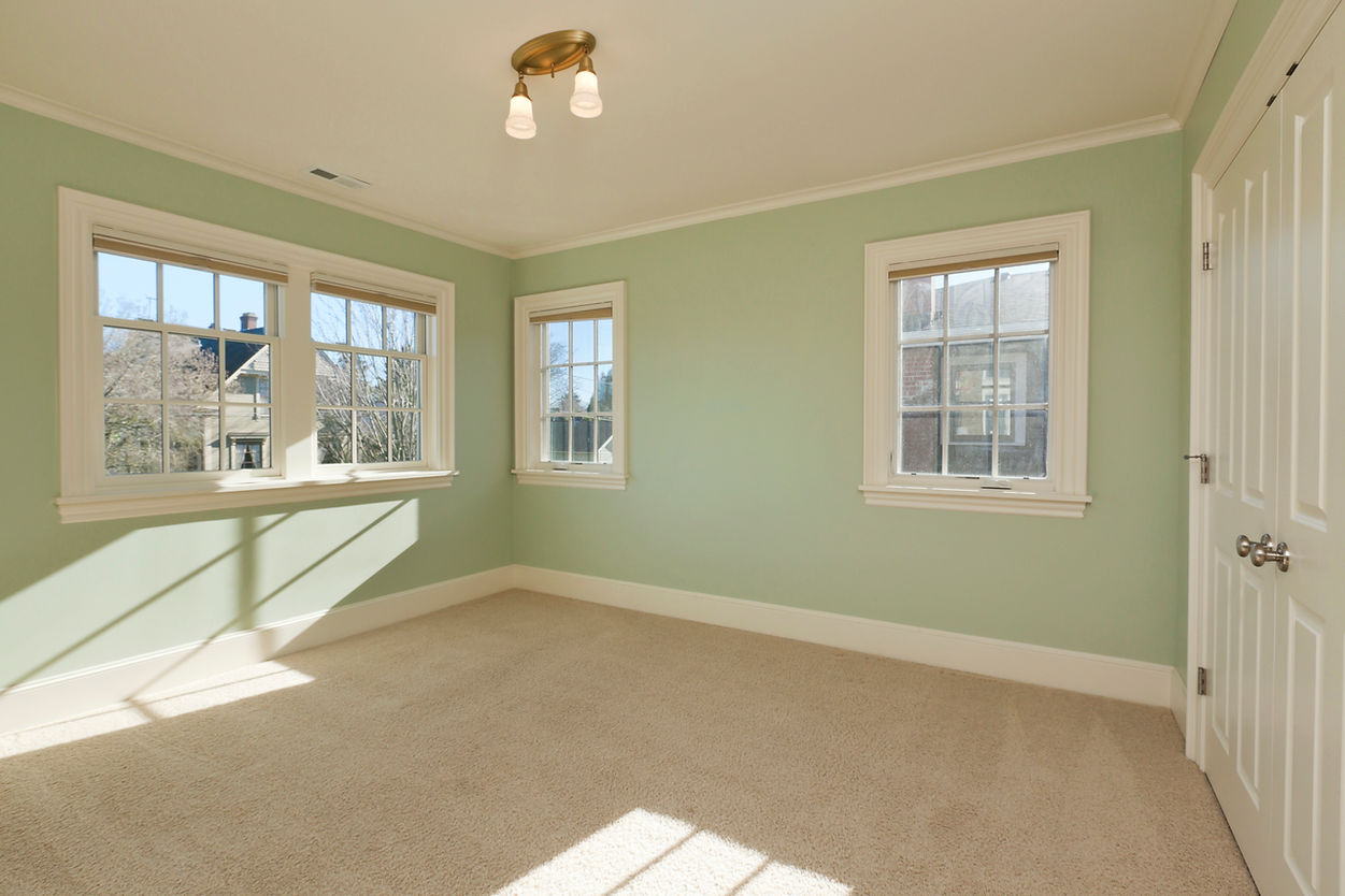 Bright, empty room with light green walls, beige carpet, and three windows on two walls