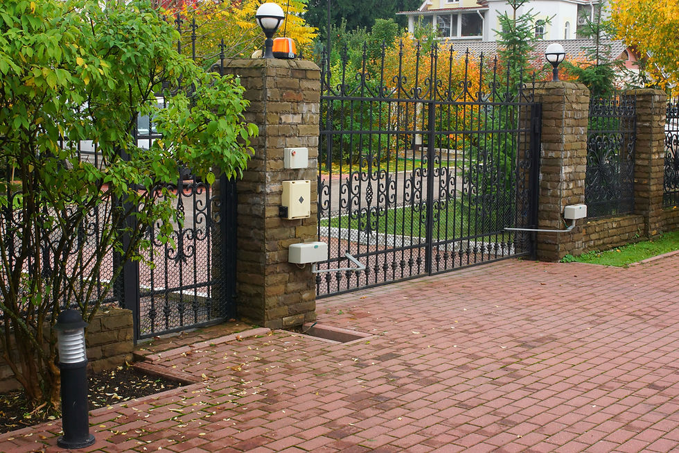 Ornamental black wrought iron driveway gates mounted on stone pillars with block paved driveway