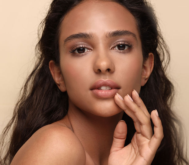 A young Hindu woman touches her face while wearing pink eyeshadow and lip tint.