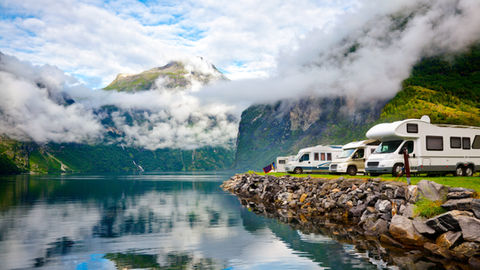 Camping-cars au bord d’un fjord calme, montagnes verdoyantes noyées de nuages se reflétant dans l’eau.