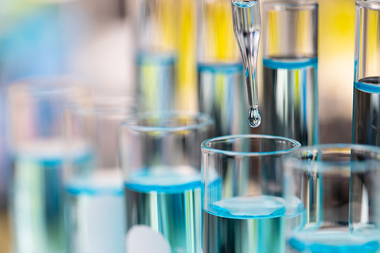 A glass pipette dripping a single liquid droplet into a laboratory vial