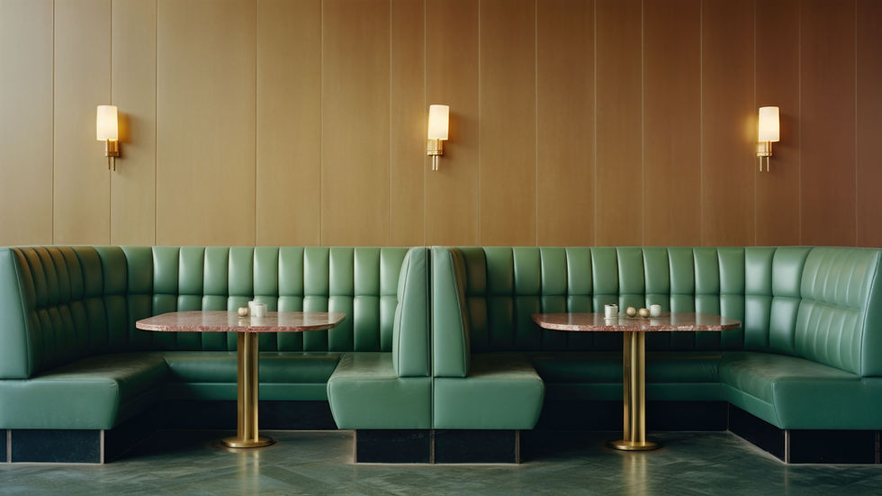 Eine moderne Restaurant Sitzecke mit grünen Polsterbänken, zwei Tischen und warmem Licht an der Wand.