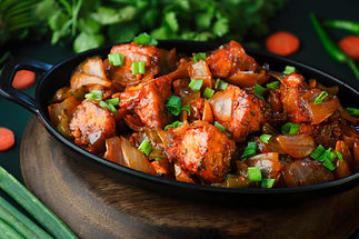 Spicy chicken curry with vibrant red sauce, garnished with green onions, served in a black dish