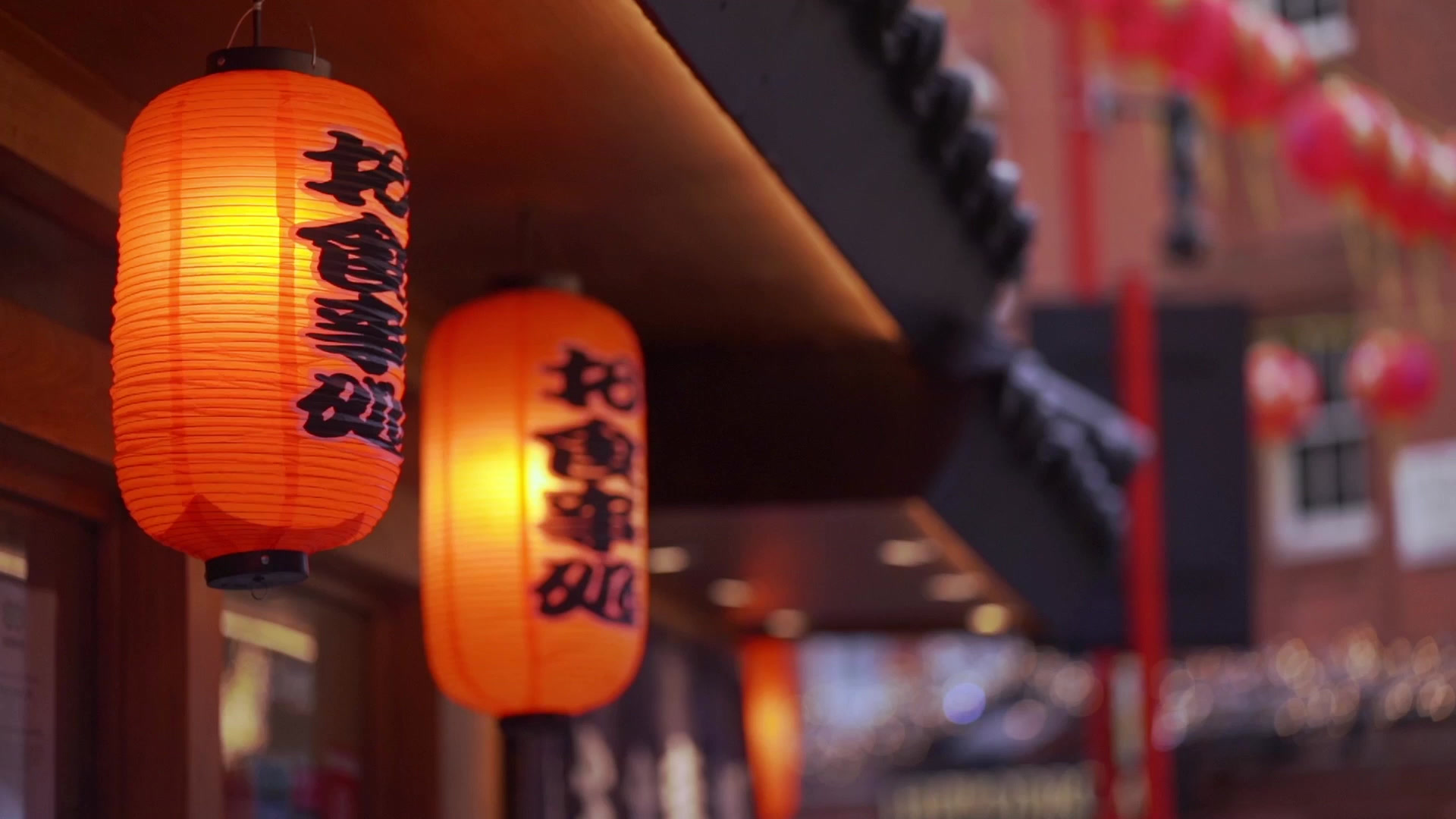 Paper lanterns glowing above a street at dusk