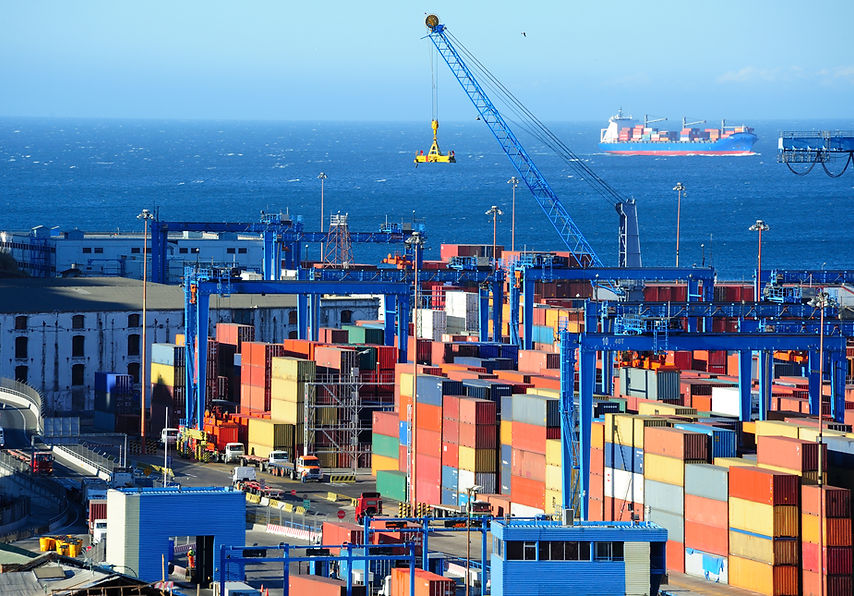Tugboat assisting a large cargo vessel entering a commercial harbour at dusk