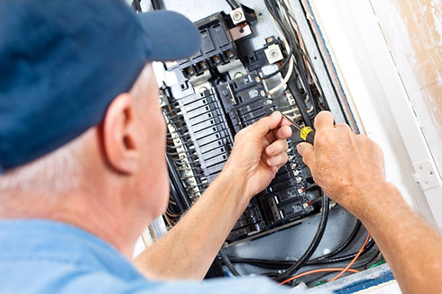 Electrician's hands using a screwdriver to work on wiring inside a fuse box