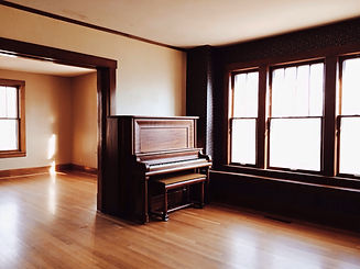 Classic dark wood upright piano in a bright room with large windows and polished wooden floors