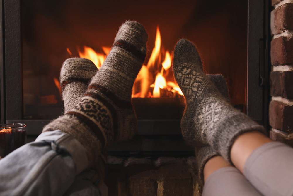 View of two people's feet in warm winter socks propped up in front of blazing fireplace.