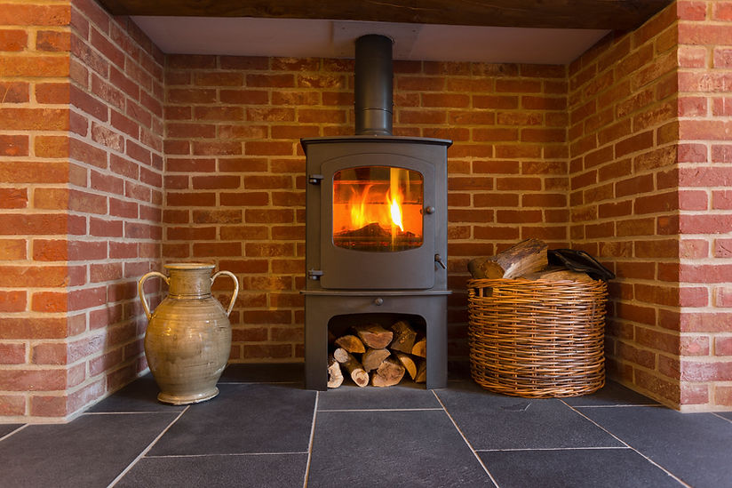 Fire in wood-burning stove in brick fireplace with basket of logs
