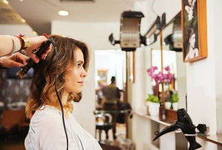 A woman with shoulder-length hair is having her hair styled with a curling iron in a salon