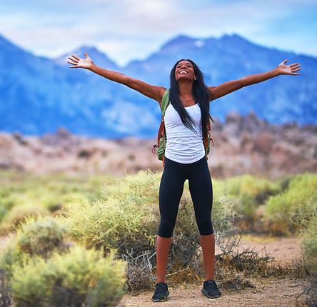 Woman standing outdoors with arms raised in joy in a mountain landscape