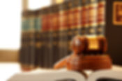 A wooden gavel rests on top of an open law book in front of a row of law books that is out