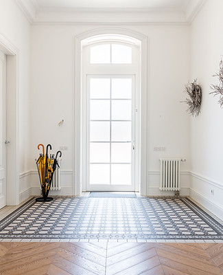 Open entryway with white walls and white front door, hard wood floor with large tiled entry way in front of door.