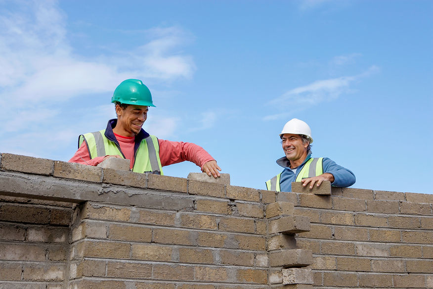 Two builders in hard hats laying bricks on a wall at a construction site