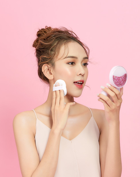 Beautiful Asian woman applying makeup with a pink background