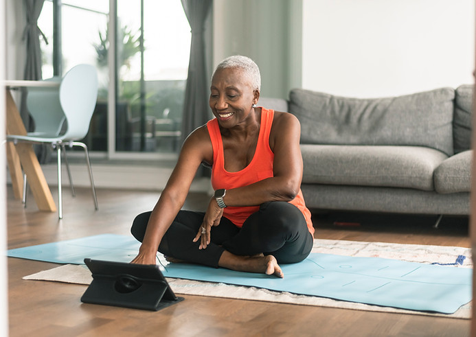 Older black woman enjoying yoga at home in her living room using a tablet and light blue yoga mat