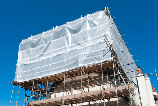 Scaffolding and white weatherproofing wrap on a building roof under a clear blue sky