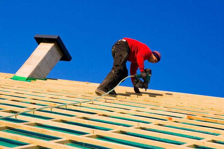 "Tilt view of a carpenter on a roof, against blue sky, carpenter building a tile batten co