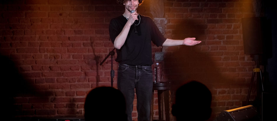 A Comedian in a darkened comedy club tells jokes to an audience