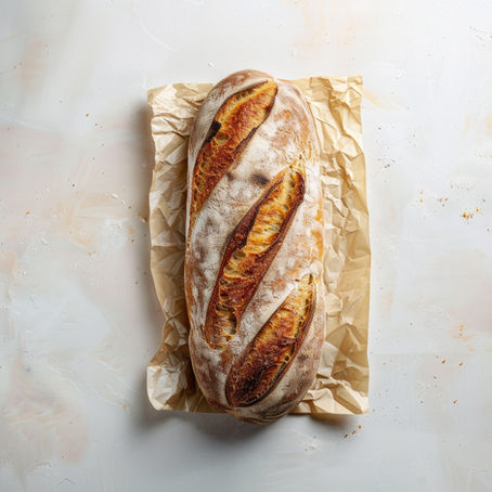 Crusty bread loaf on crinkled parchment paper against a textured white background. The loaf has slashes and a golden-brown crust.