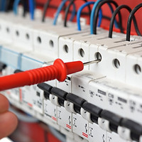 A multimeter probe testing an electrical circuit breaker panel
