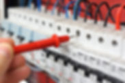 Hand of an electrician with multimeter probe at an electrical switchgear cabinet