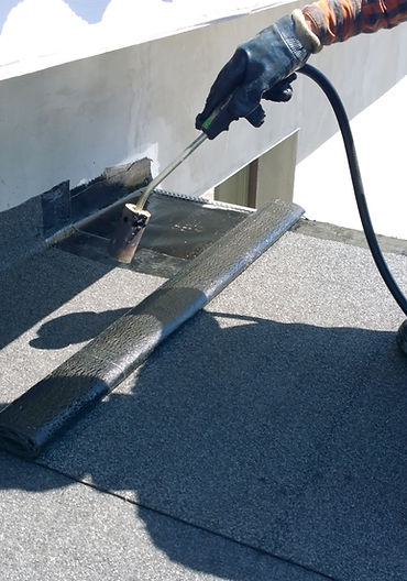 Roofer preparing part of bitumen roofing felt roll for melting by gas heater torch flame
