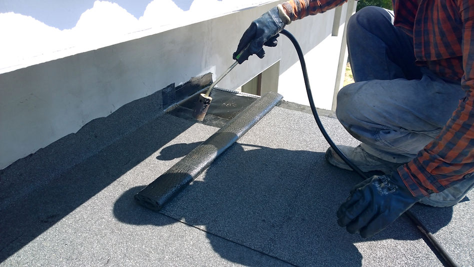 Roofer using a gas torch to heat-weld a layer of bituminous felt onto a flat roof