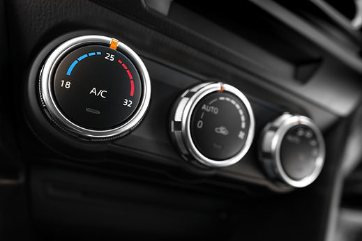 Close-up of three black car air conditioning control knobs with silver trim on a dark dashboard
