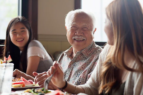 Grandfather is eating a meal with his granddaughters.