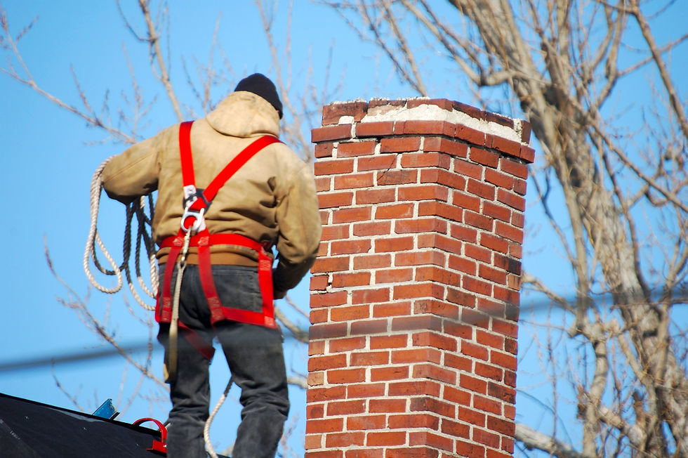Roof worker wearing a red safety harness repairing a tall red brick chimney against a blue sky