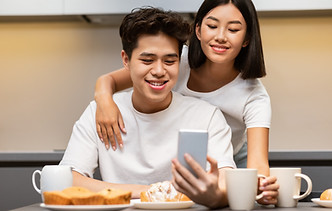Happy newlywed Asian couple watching something on their smartphone together