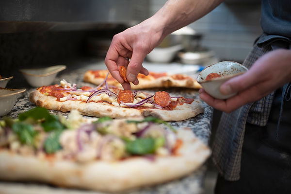 Pizza-Zubereitungsszene zeigt wie frischer Pizzateig belegt wird