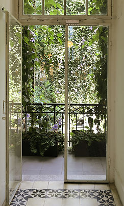 Widok z wnętrza na balkon z roślinami pnącymi się po balustradzie i skrzynkach kwiatowych