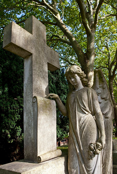 A stone angel with wings and gentle expression leans against a large cross in a cemetery